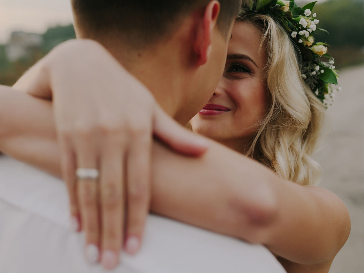 A couple is embracing each other, with the woman wearing a floral headband and showing a ring on her finger.