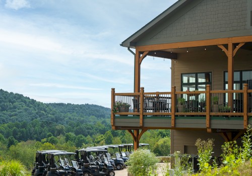 A scenic view of a golf clubhouse with a wooden balcony overlooking several golf carts and lush green hills in the background, ending the sentence.