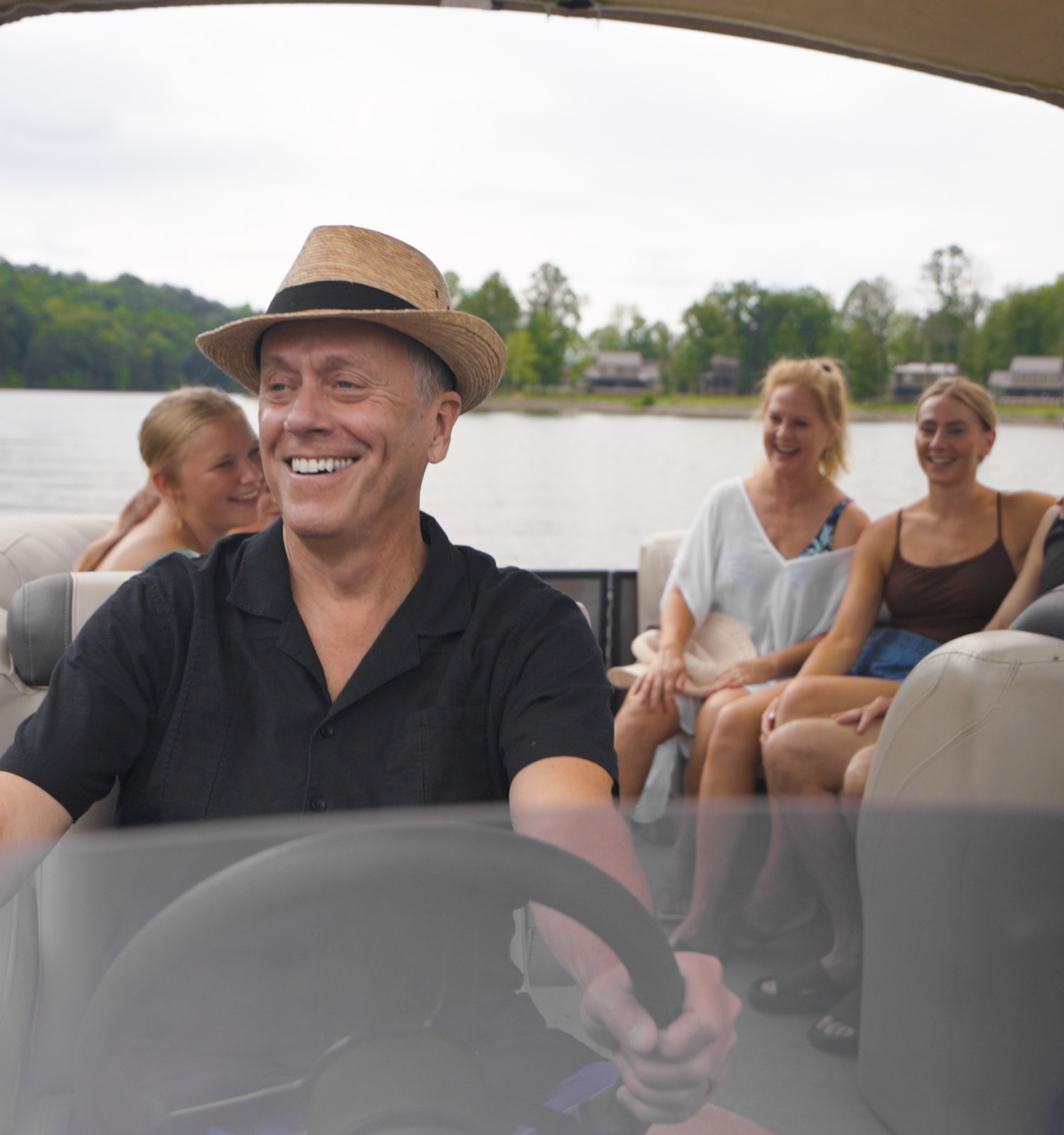 A group of friends enjoys a boat ride on a lake, laughing and relaxing with nature and nearby houses in the background.