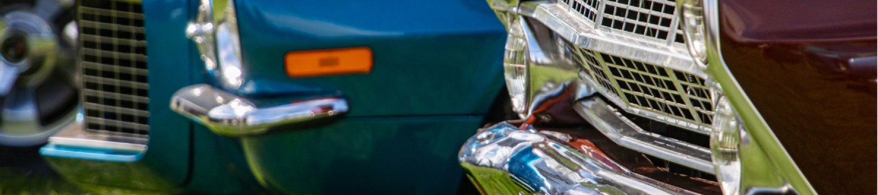 The image shows the front ends of two classic cars, one blue and one maroon, parked on grass.