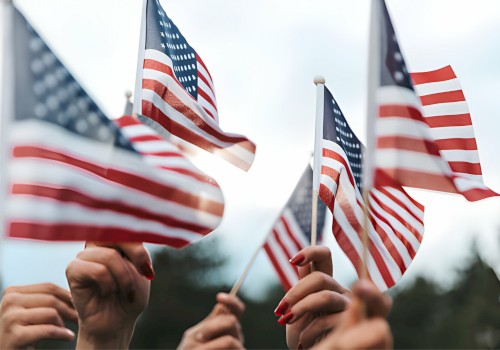 People are holding multiple American flags raised high against a blurred outdoor background, creating a sense of unity and patriotism.