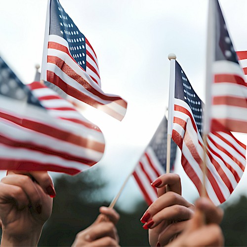 People are holding multiple American flags raised high against a blurred outdoor background, creating a sense of unity and patriotism.