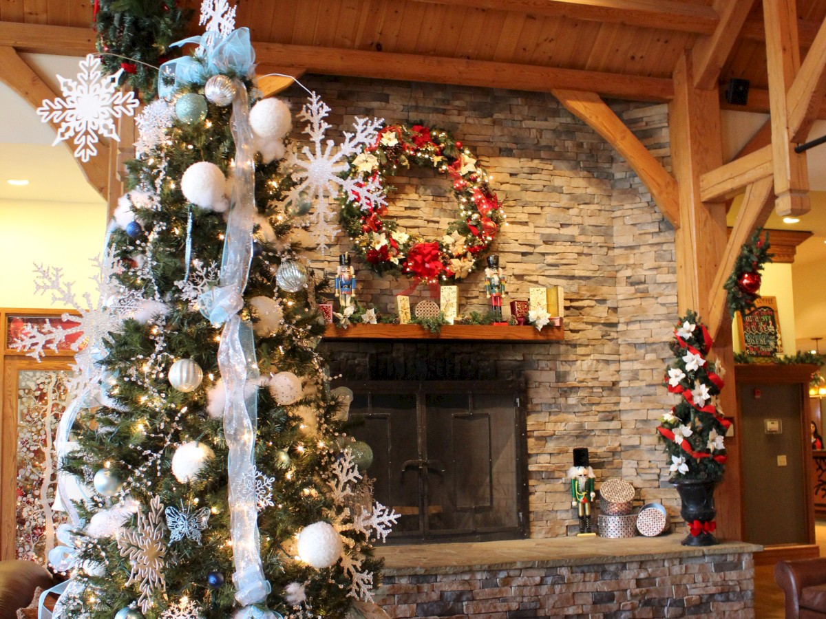 The image features a cozy, festive room with a decorated Christmas tree, a wreath above a stone fireplace, and wooden ceiling beams.