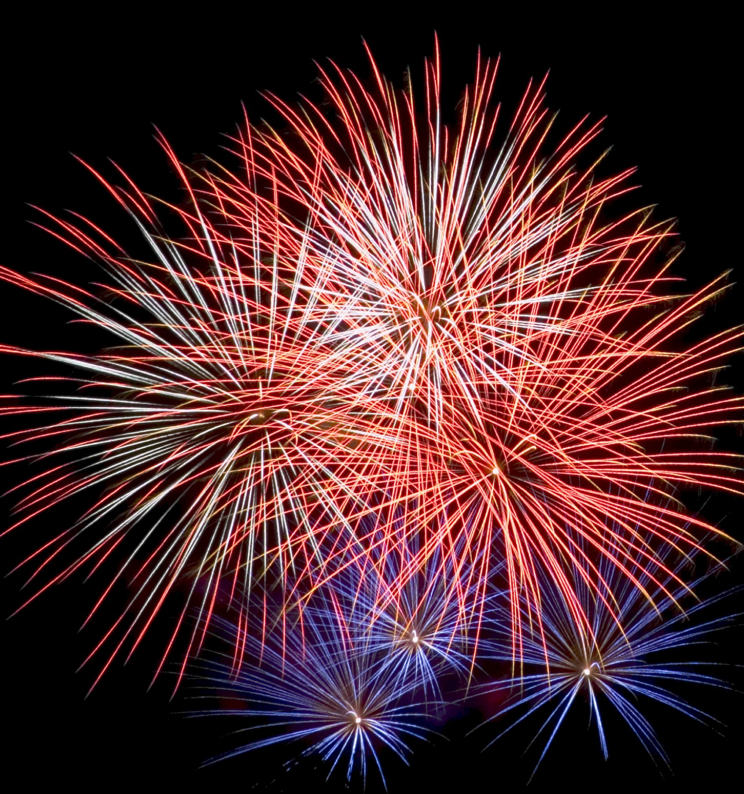 The image shows a colorful display of fireworks bursting in the night sky with red, white, and blue colors creating striking patterns.