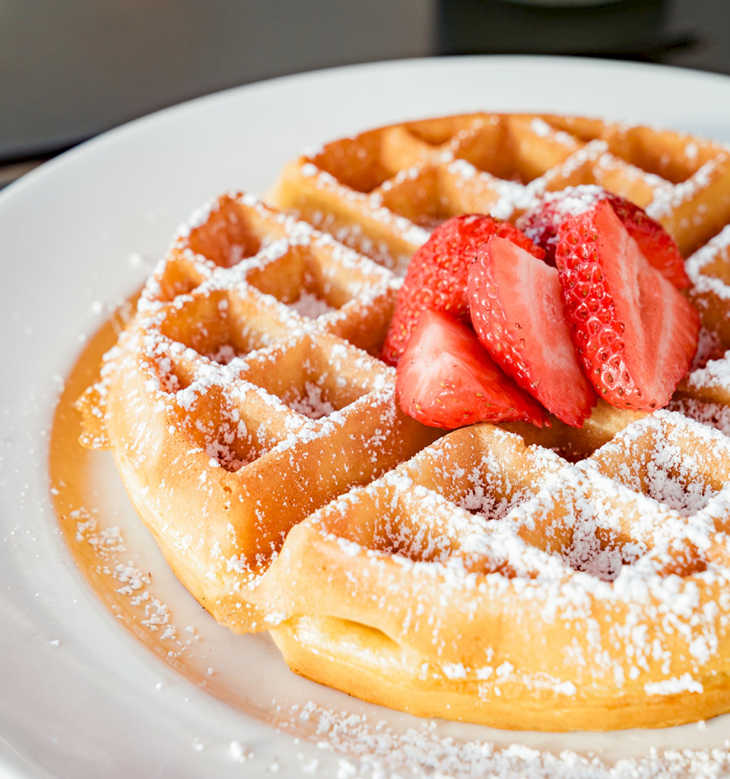 A plate of waffles topped with powdered sugar and fresh strawberry slices, served on a white plate.