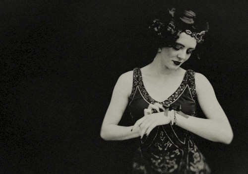 The image shows a person dressed in a vintage style, possibly from the early 20th century, looking down while adjusting something on their wrist.