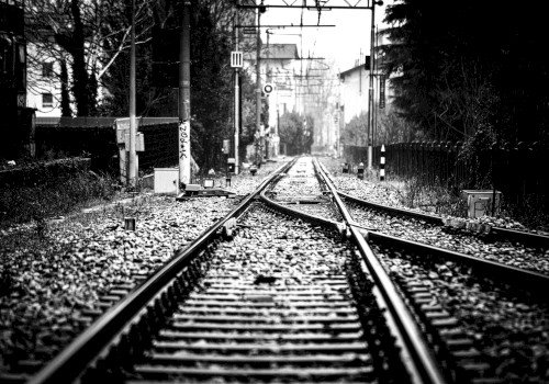 The image shows a black-and-white view of railway tracks with surrounding trees and buildings, and the tracks are converging in the distance.