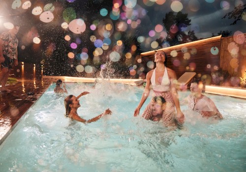 People are enjoying a night at the pool, with colorful lights creating a festive atmosphere. Some are in the water, splashing around.