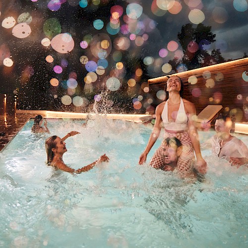 People are enjoying a night at the pool, with colorful lights creating a festive atmosphere. Some are in the water, splashing around.