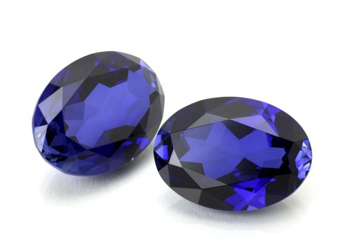 The image shows two oval-shaped, faceted blue gemstones placed on a white surface.