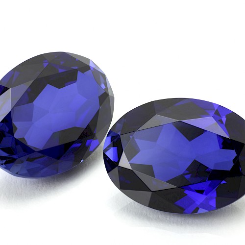 The image shows two oval-shaped, faceted blue gemstones placed on a white surface.