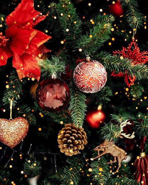 The image shows a decorated Christmas tree with red ornaments, bows, pine cones, and golden lights, creating a festive atmosphere.