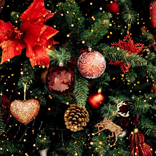 The image shows a decorated Christmas tree with red ornaments, bows, pine cones, and golden lights, creating a festive atmosphere.