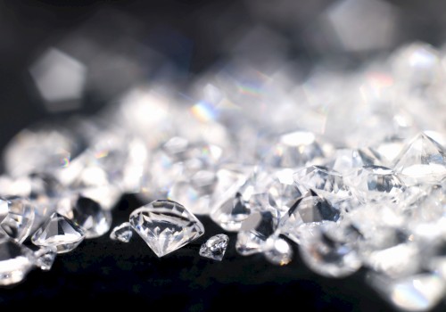 The image displays a collection of sparkling diamonds scattered on a dark surface, with some out of focus in the background.