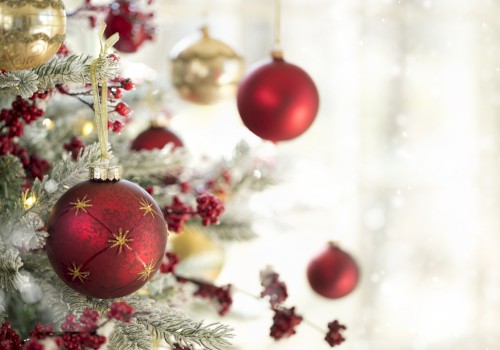 A decorated Christmas tree with red and gold ornaments, pine cones, and frosted branches, in a softly lit and snowy background.