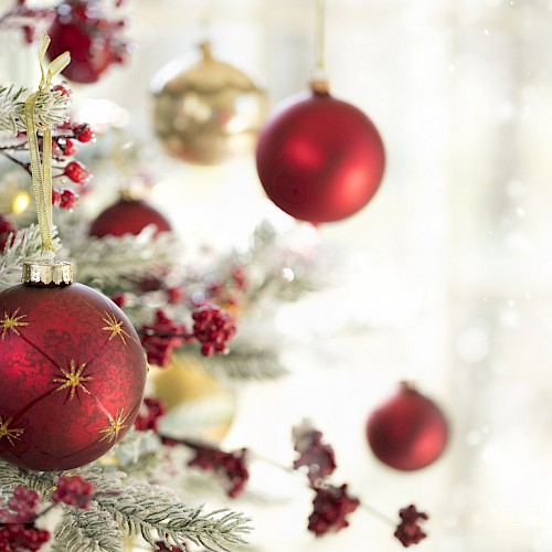 A decorated Christmas tree with red and gold ornaments, pine cones, and frosted branches, in a softly lit and snowy background.