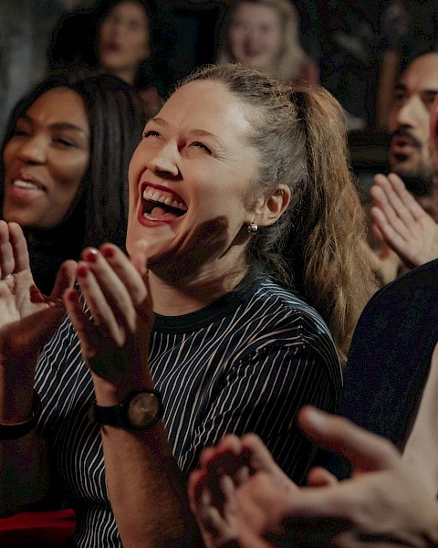 A group of people is clapping and laughing, appearing to enjoy a show or performance in a lively and cheerful atmosphere.