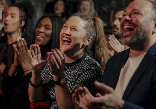 A group of people is clapping and laughing, appearing to enjoy a show or performance in a lively and cheerful atmosphere.