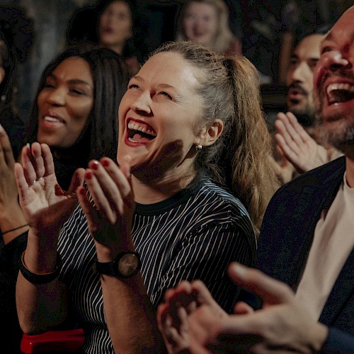 A group of people is clapping and laughing, appearing to enjoy a show or performance in a lively and cheerful atmosphere.