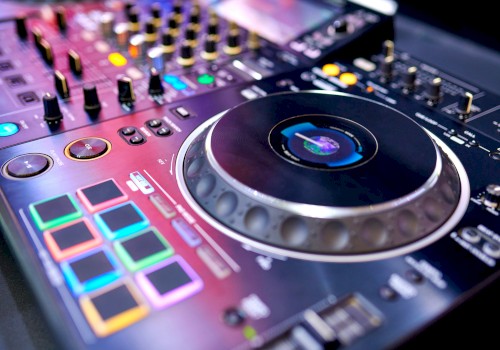 The image shows a close-up of a DJ controller with colorful pads, dials, and a large jog wheel, used for mixing music.