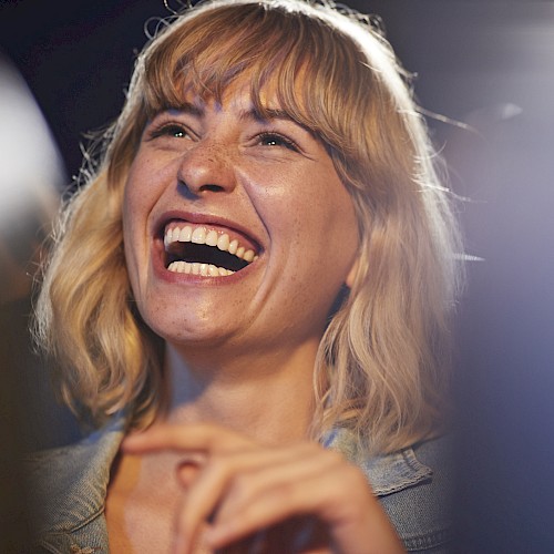 A person with blonde hair is laughing joyfully in a candid moment. The background is slightly blurred.