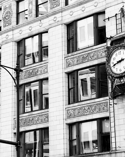 A historic building corner with ornate architecture features a large clock. Streetlights and a street sign are visible in black and white.