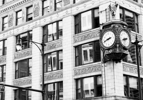 A historic building corner with ornate architecture features a large clock. Streetlights and a street sign are visible in black and white.