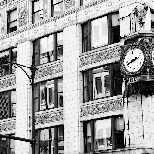 A historic building corner with ornate architecture features a large clock. Streetlights and a street sign are visible in black and white.