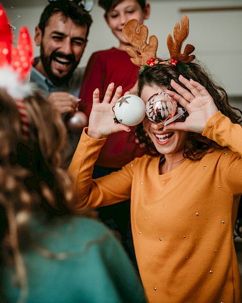 A group of people enjoying a festive moment indoors, with one person holding ornaments to their eyes, and others smiling in the background.