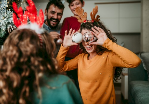 A group of people enjoying a festive moment indoors, with one person holding ornaments to their eyes, and others smiling in the background.