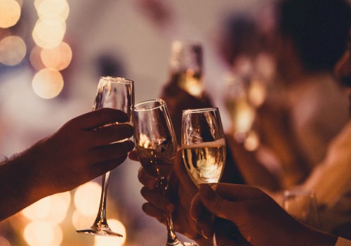 People are holding and clinking champagne glasses at a celebration, with warm, blurred lights in the background.