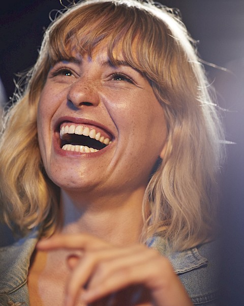 A person with blonde hair is laughing joyfully in a candid moment. The background is slightly blurred.