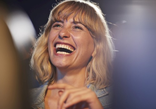 A person with blonde hair is laughing joyfully in a candid moment. The background is slightly blurred.