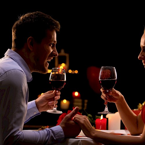 A couple enjoying a romantic candlelit dinner, holding glasses of red wine and smiling at each other.