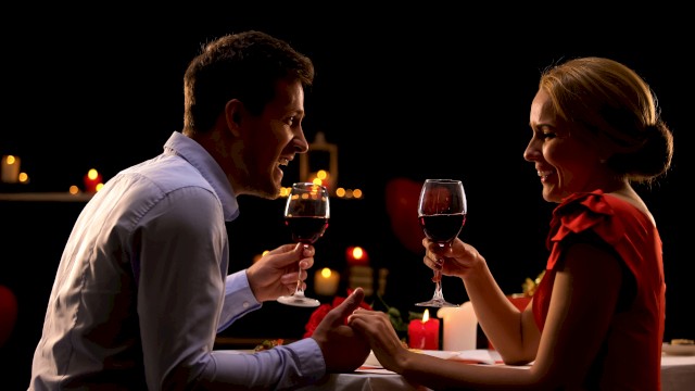 A couple enjoying a romantic candlelit dinner, holding glasses of red wine and smiling at each other.
