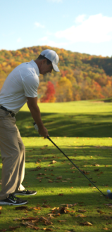 A person is preparing to hit a golf ball on a lush course with autumn trees in the background.