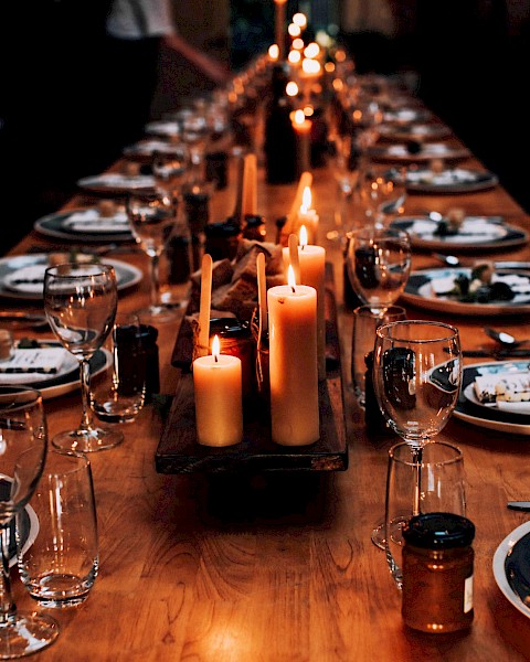 A long dining table is elegantly set with plates, cutlery, glasses, and lit candles, creating a warm, inviting atmosphere.