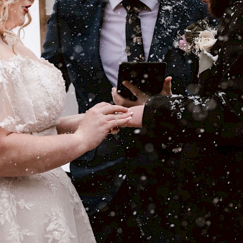 A couple exchanging rings during an outdoor wedding ceremony in the snow, accompanied by an officiant holding a book.