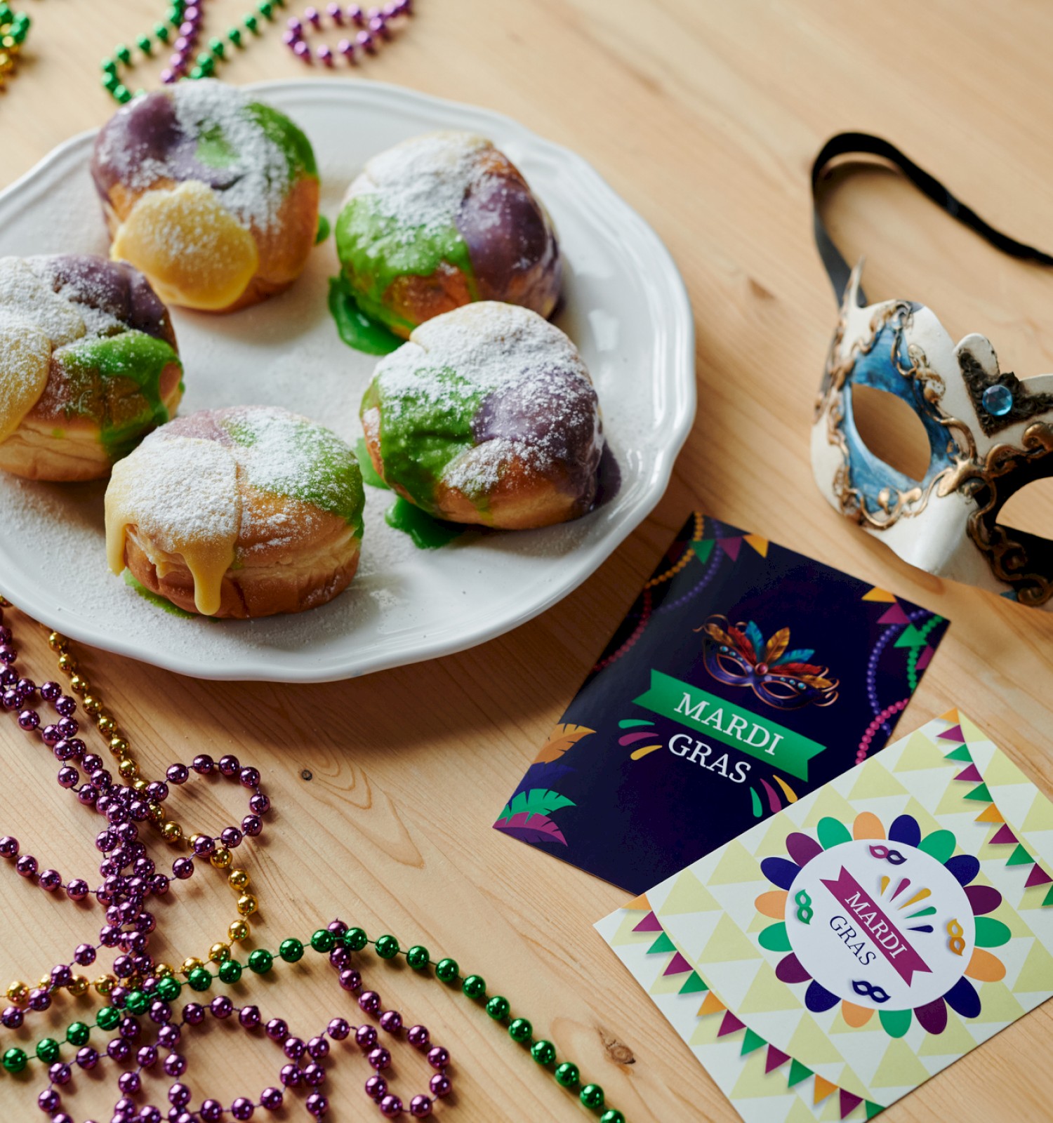 A table with Mardi Gras donuts, colorful beads, a mask, and themed cards, embodying a festive celebration.