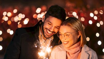 A couple is joyfully holding sparklers at night, surrounded by blurry festive lights, creating a romantic ambiance.