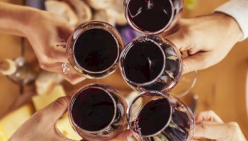 People are raising wine glasses over a table with food, including bread and meats, suggesting a celebration or gathering.