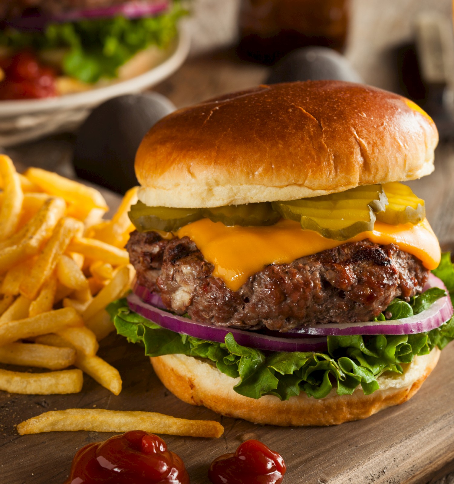 A cheeseburger with lettuce, onion, pickles, and fries on a wooden board, accompanied by a glass of beer. Ketchup is on the side.