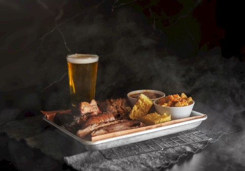 The image shows a tray of smoked meats, various sides, and a glass of beer, creating a hearty meal setting.