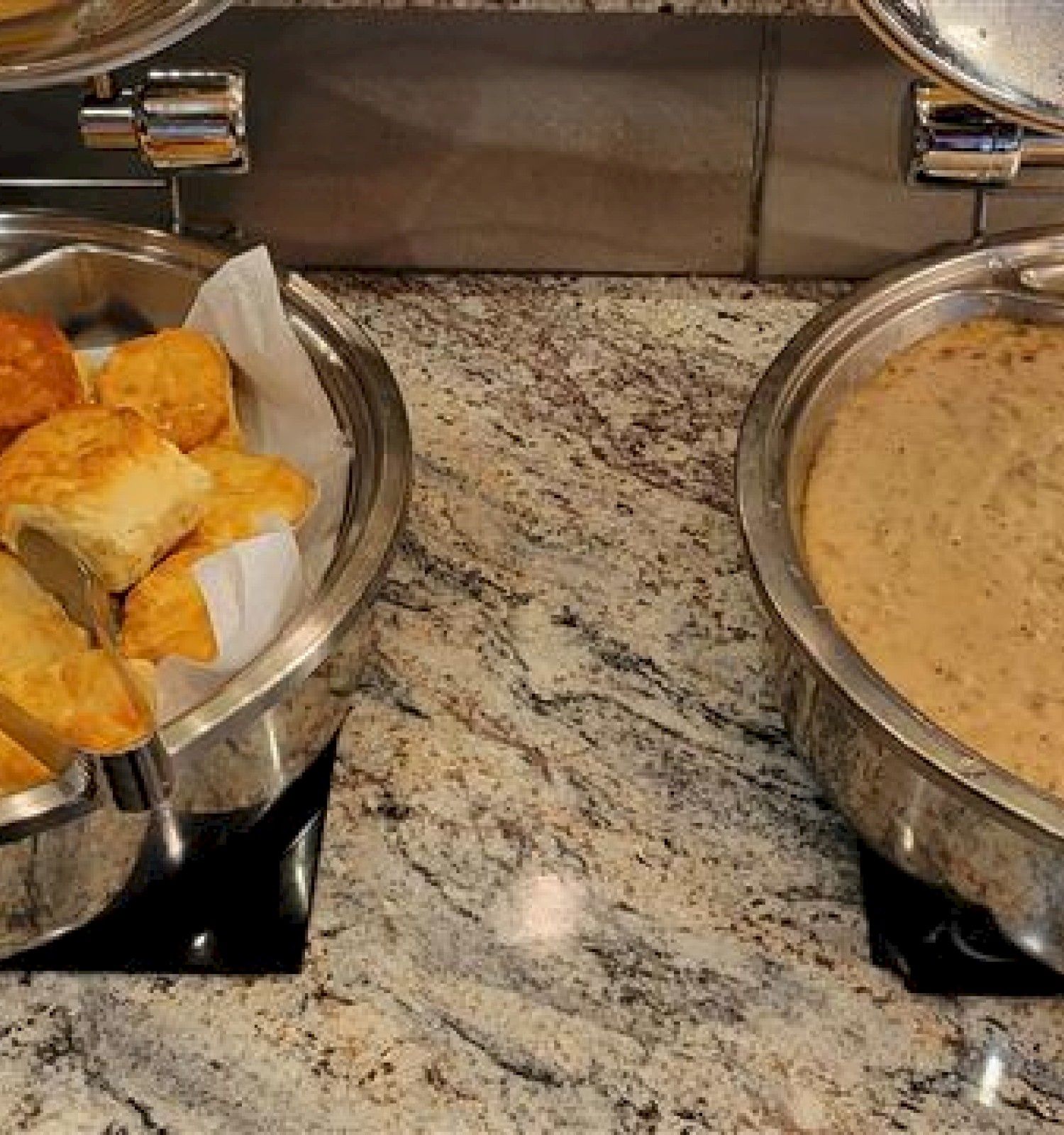 Cheesy biscuits or scones on the left and a creamy beige soup or chowder in a stainless warmer on the right, set on a granite counter.