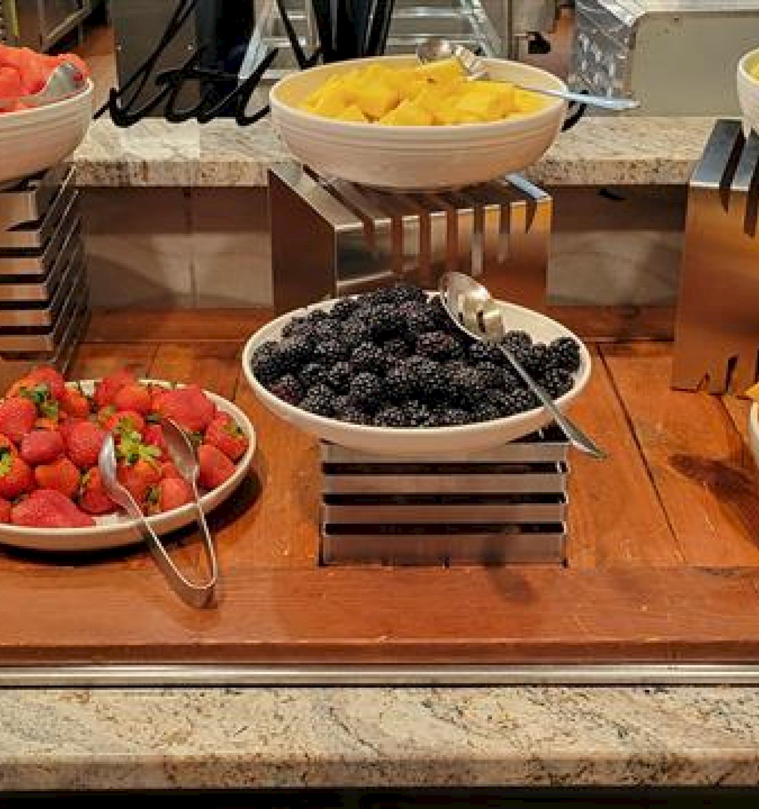 Fresh fruit bowls on a buffet: blueberries, strawberries, blackberries, melon, pineapple, kiwi, and diced cantaloupe, all neatly arranged.