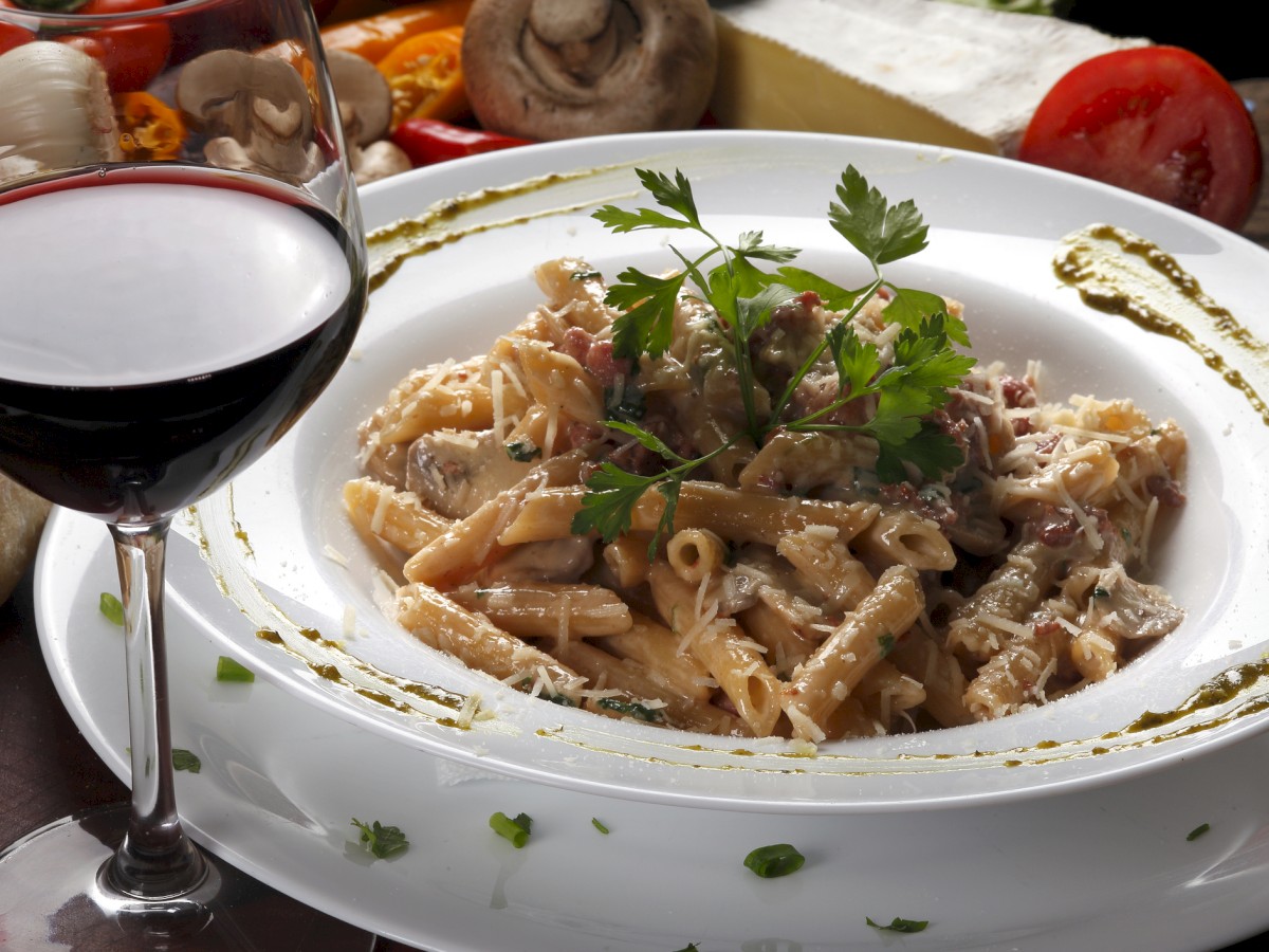 A plate of creamy pasta garnished with parsley, surrounded by ingredients, paired with a glass of red wine.