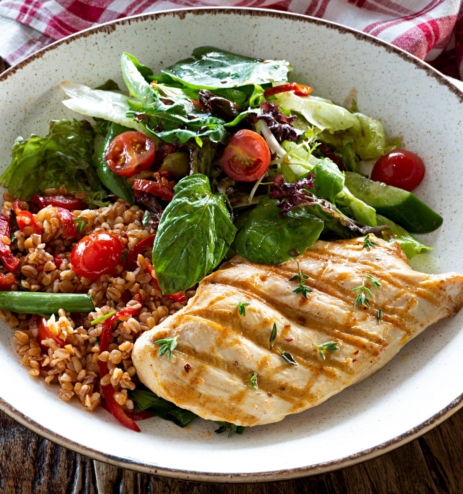 Grilled chicken breast with a side of mixed salad and seasoned rice, served on a rustic plate with a plaid cloth backdrop.