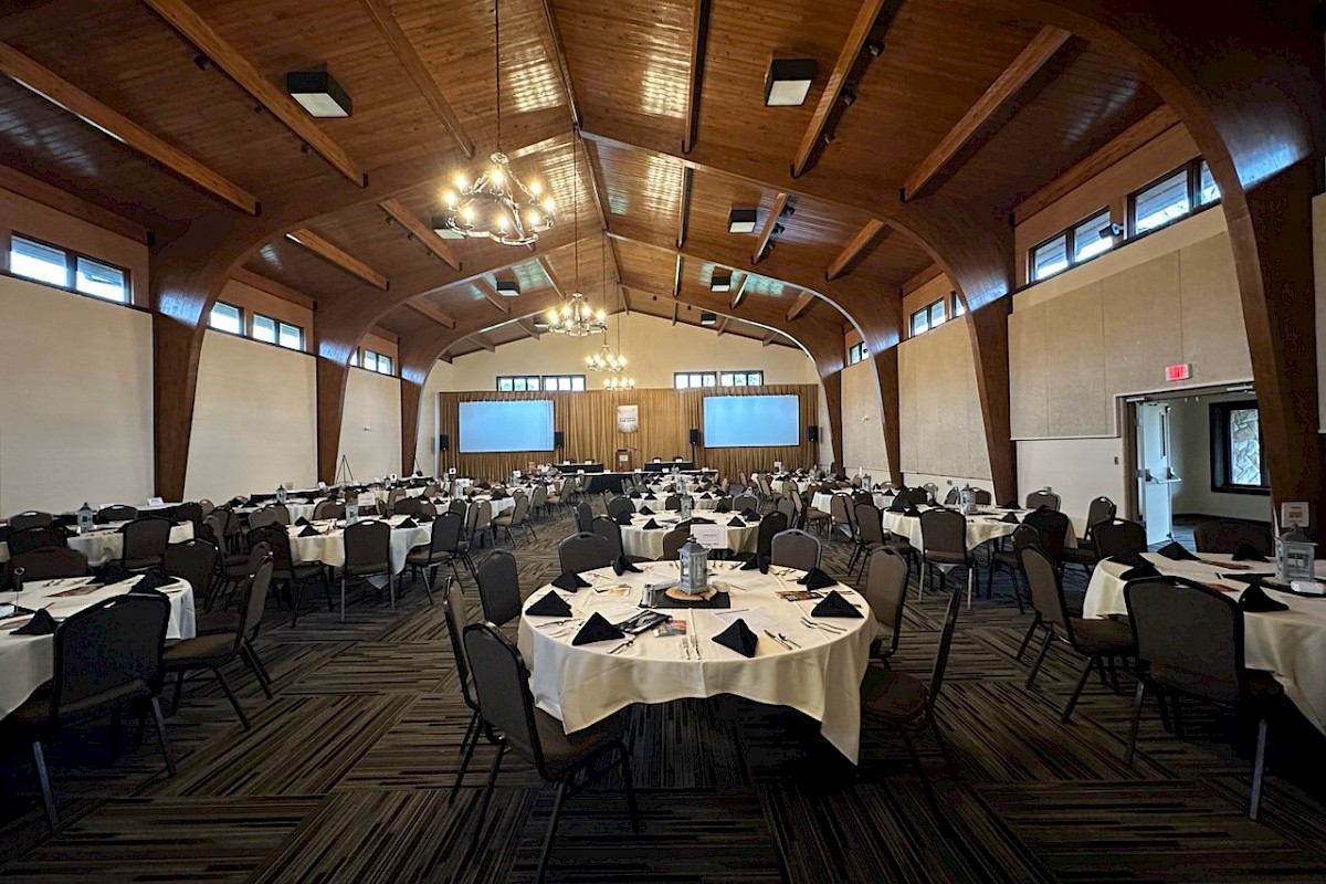 The image shows an elegant banquet hall with round tables set with white tablecloths, black napkins, and surrounded by chairs.