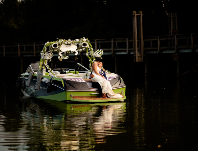 A couple in wedding attire sits on a boat decorated with flowers and a 