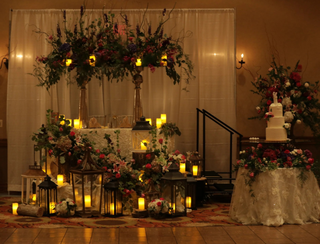 A beautifully decorated wedding setup with floral arrangements, candles, lanterns, and a multi-tiered cake on a table.